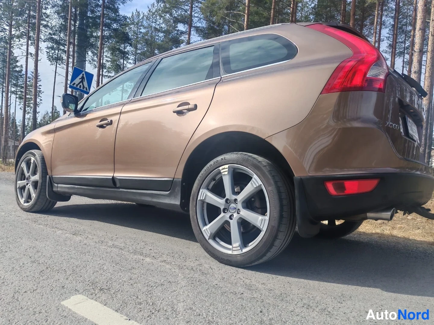 Takaviisto: Ruskea farmarimallinen automme takakulmasta, takavalo ja takapyörä näkyvät tien varrella.