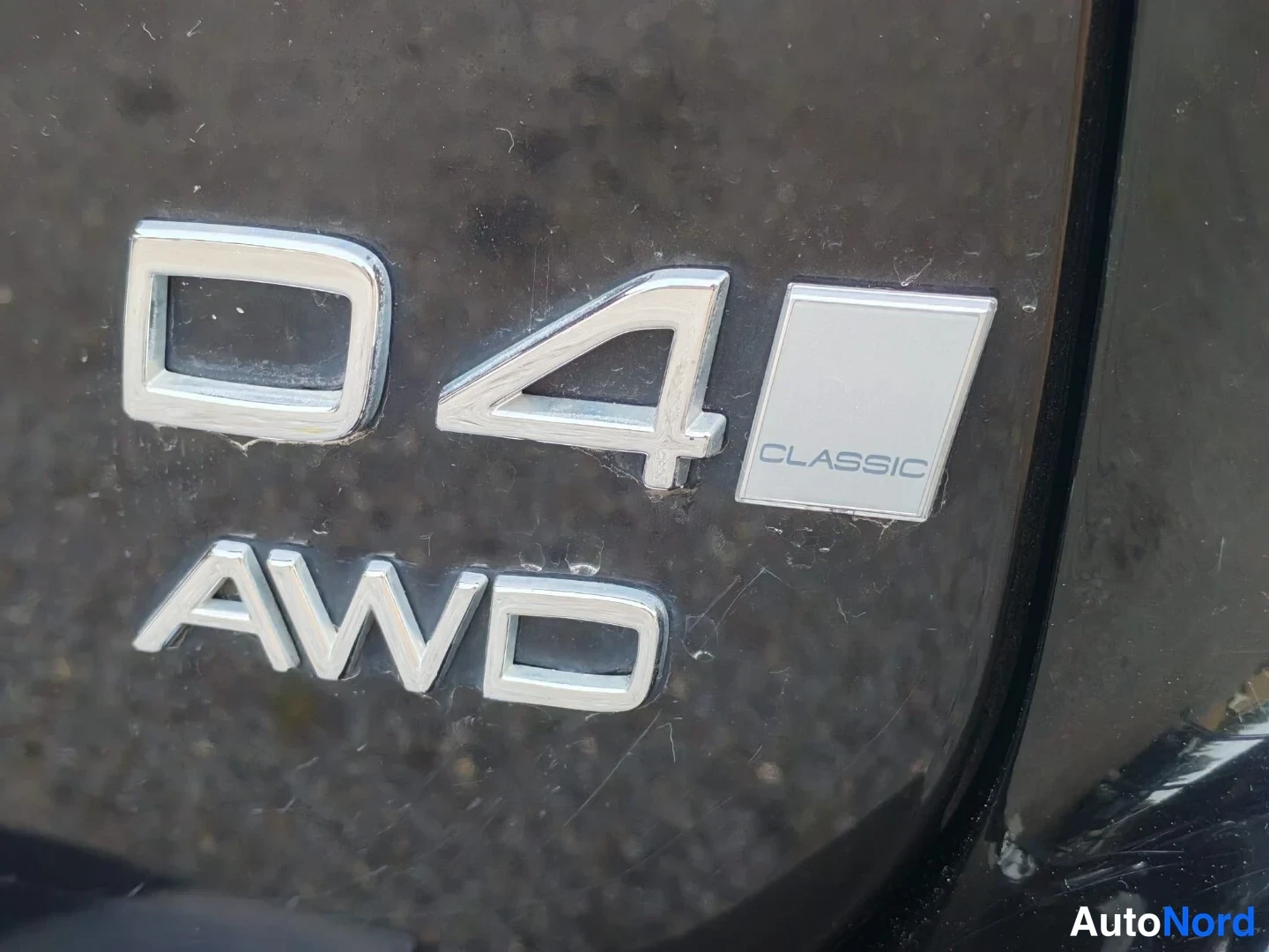 Yksityiskohta: Close-up of chrome 'D4 CLASSIC AWD' emblems on a dark vehicle body panel.