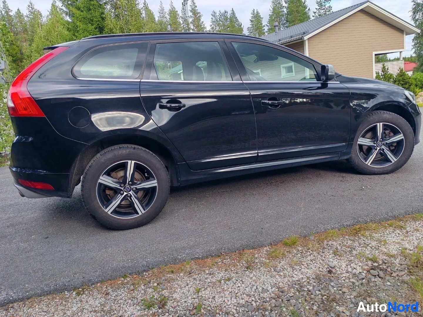 Takaviisto: Musta farmuri autotallin pihalla, takakolmasosan näkymä vasemmalta: takavalot, tavaratilan kansi ja pyörät näkyvissä.