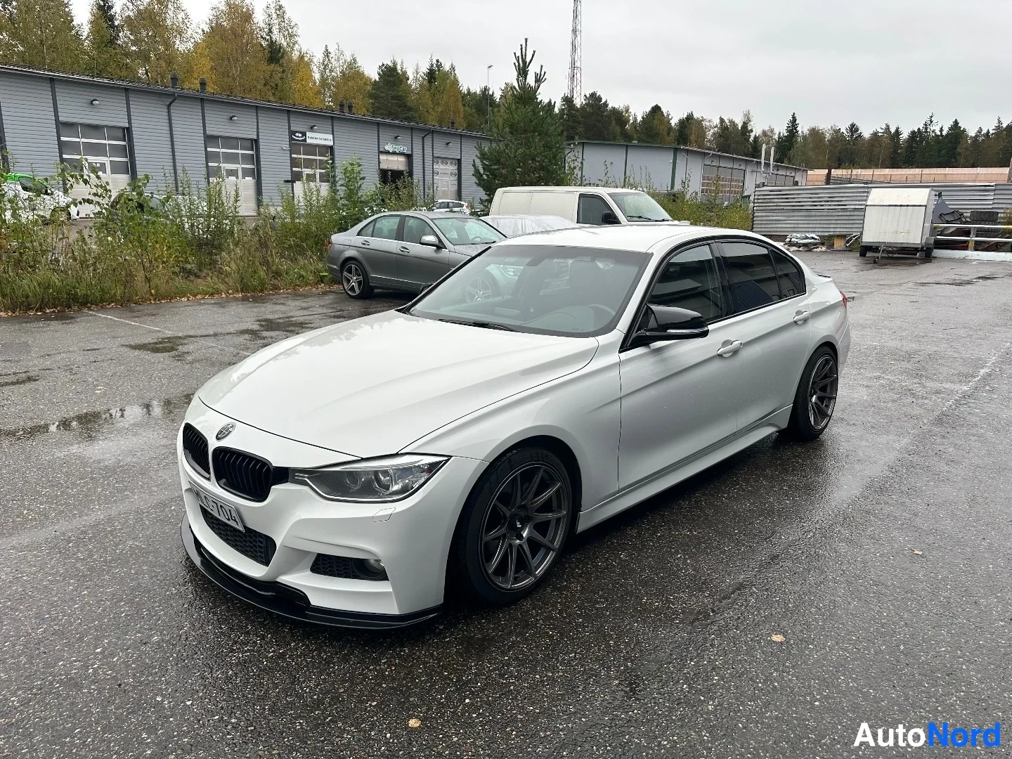 Etuviisto, nokka vasemmalle: Valkoinen BMW-sedan ulkona paikallispaikalla, auton keula osoittaa vasemmalle, tummat vanteet ja musta etusplitteri.