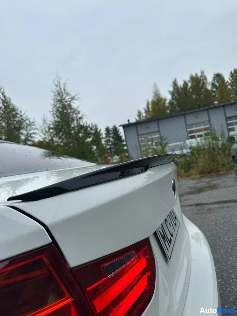 Takaa: Lähikuva valkoisen auton takaluukusta: musta spoileri takaluukun reunassa, punaiset takavalot ja osittain näkyvä rekisterikilpi.