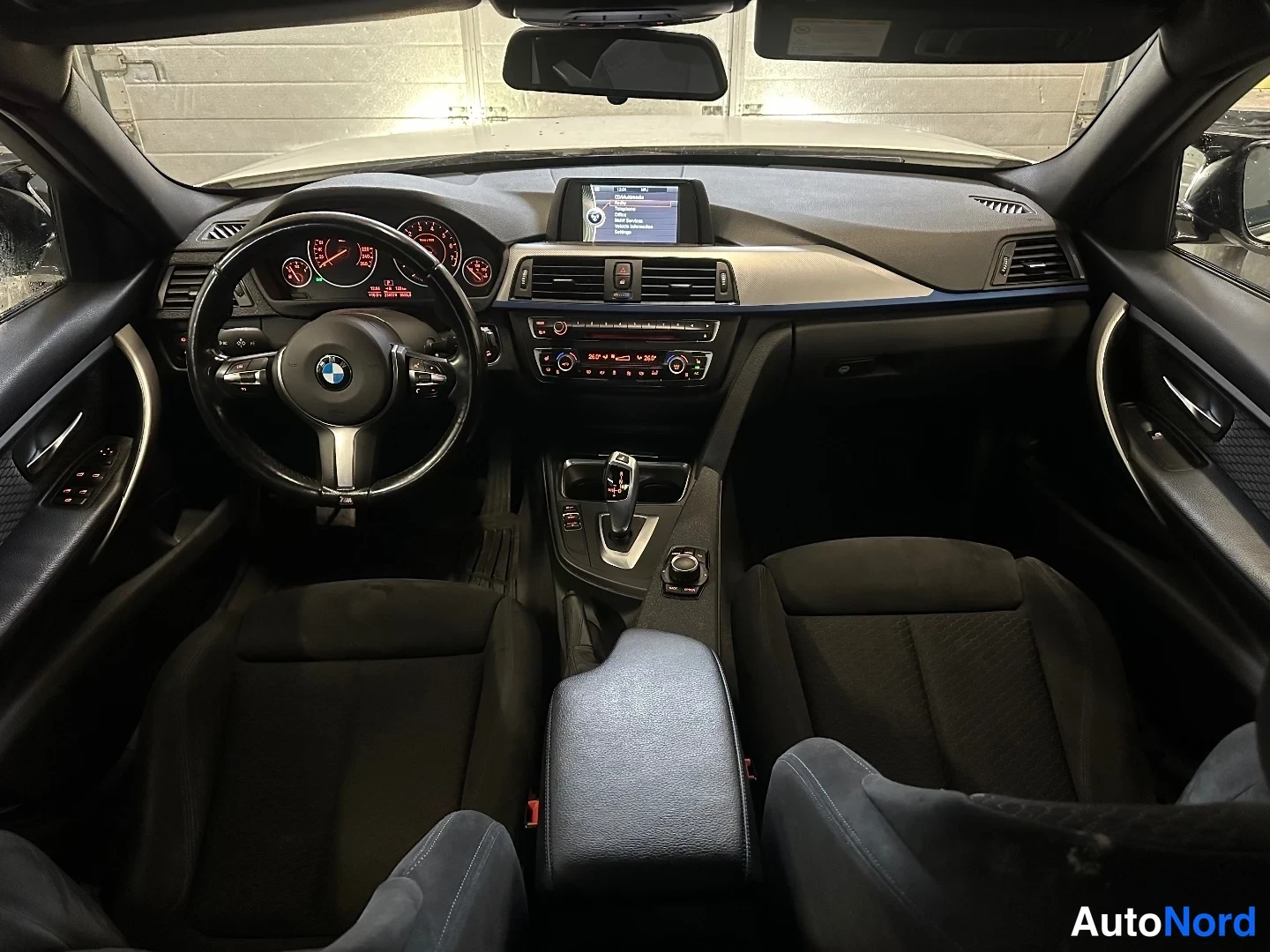 Yksityiskohta: Auton sisätilat ohjaamosta kuvattuna: BMW-ohjauspyörä, kojelauta mittareineen, keskikonsolin näyttö ja automaattivaihteen valitsin, kaksi etuistuinta.