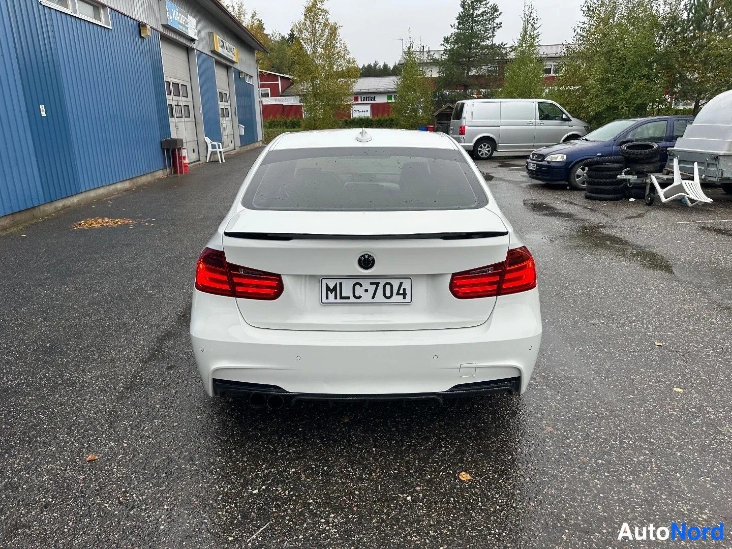 Takaa: Valkoisen BMW:n takaosa suoraan takaa; rekisteritunnus, kaksi pakoputkea ja takavalo näkyvissä.