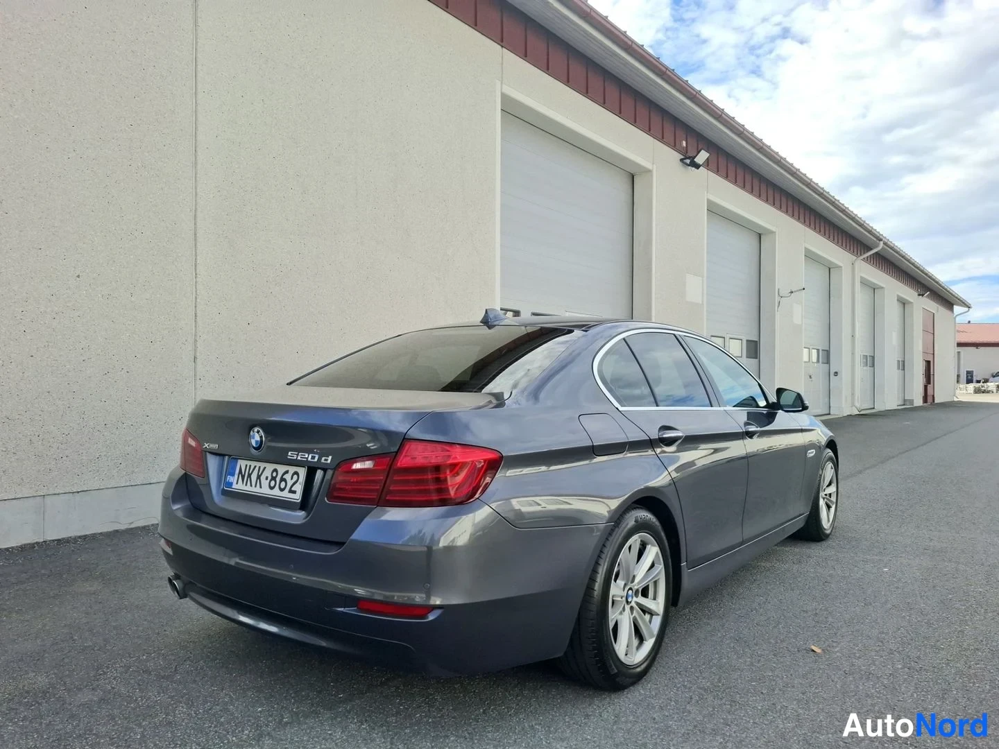 Takaviisto: Tummanharmaa BMW-sedan takakolmannes vasemmalta, rekisteritunnus, mallimerkintä 520d takaluukussa.