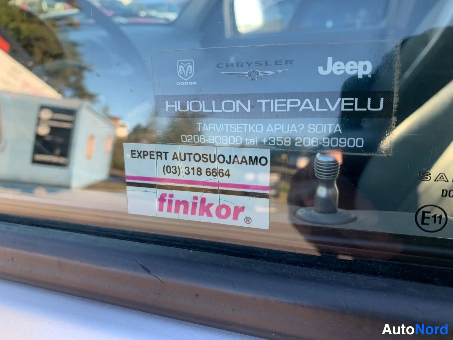 Edestä: Tuulilasin sisäpuolen tarrat: huoltotiepalvelutiedote ja Expert Autosuojaamo -finikor-tarrale.