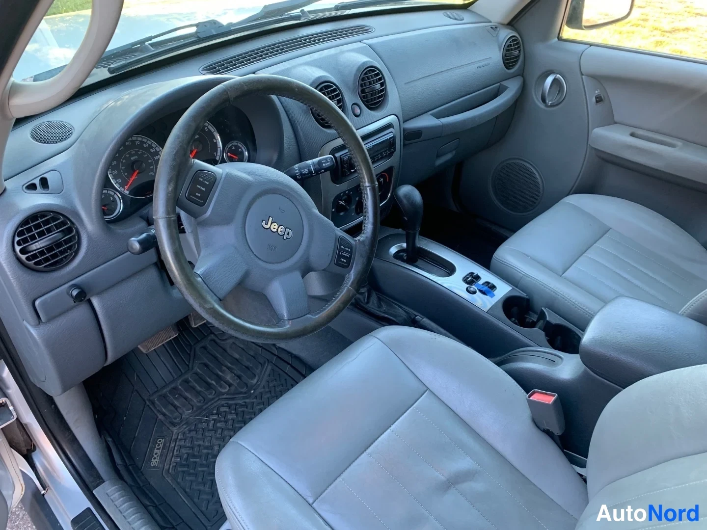 Muu: Ohjaamo vasemmalta ohjaamosta: Jeep-ohjauspyörä, mittaristo, automaattivaihteen valitsin ja harmaat istuimet.