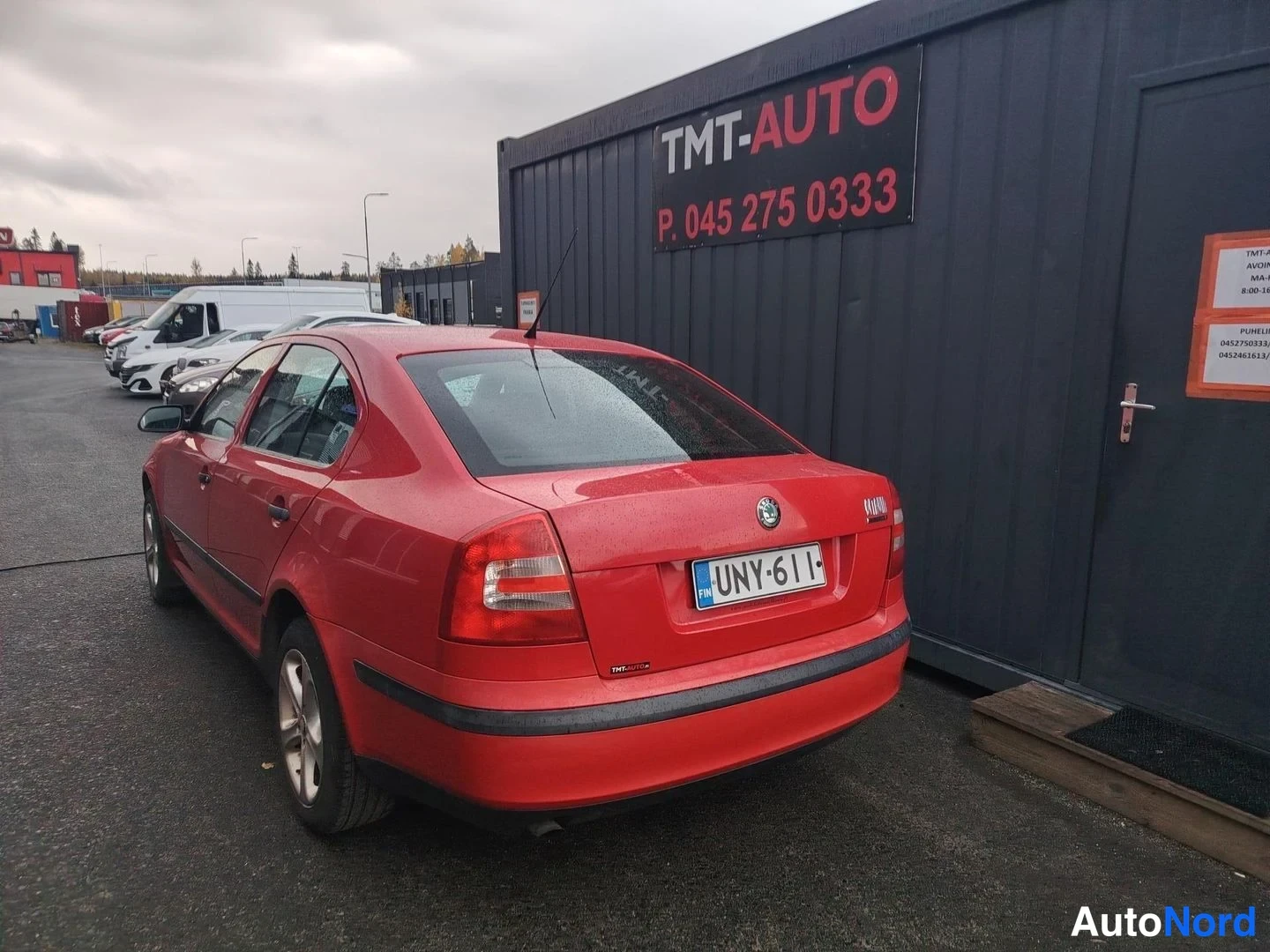 Takaviisto: Punaisen sedan takakulma, rekisteritunnus, Skoda-tunnuksella takaluukussa, TMT-Auton kontti oikealla.