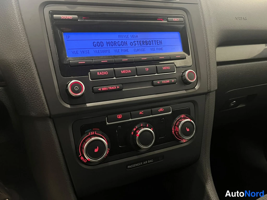 Muu: Keskikonsolin radio ja ilmastointipaneeli; radion näytöllä teksti 'GOD MORGON ÖSTERBOTTEN', AC-näppäin ja PASSENGER AIR BAG -tarra näkyvät.