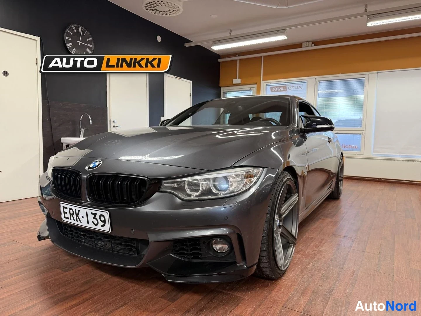 Etuviisto, nokka oikealle: Harmaansininen BMW-kuppa sisätilassa, etualalla ja vasemmassa sivussa nähtävänä. Etusuihkut LED-valoja. Tunnettu takakatto ja rekisterikilpi. Alumiini-va