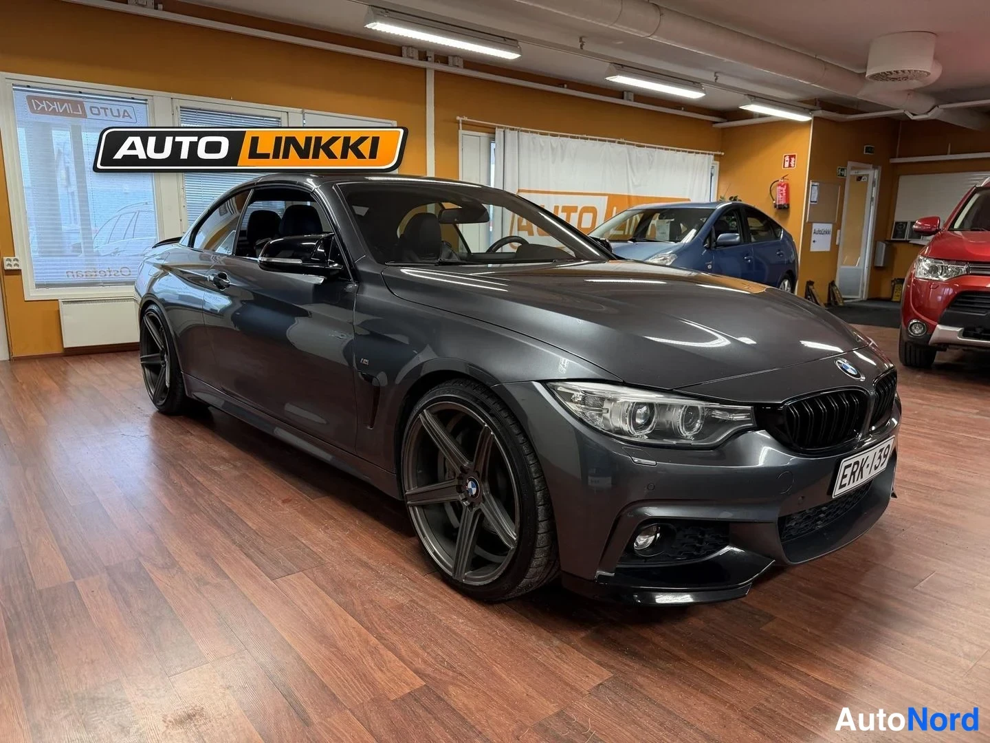 Etuviisto, nokka vasemmalle: Harmaansininen BMW-avoin auto autotallissa, oikeasta kulmasta kuvattuna. Edeisessä grilli, LED-etusoojien ja takakaton näkyvissä. Alumiini-vanteet. Har