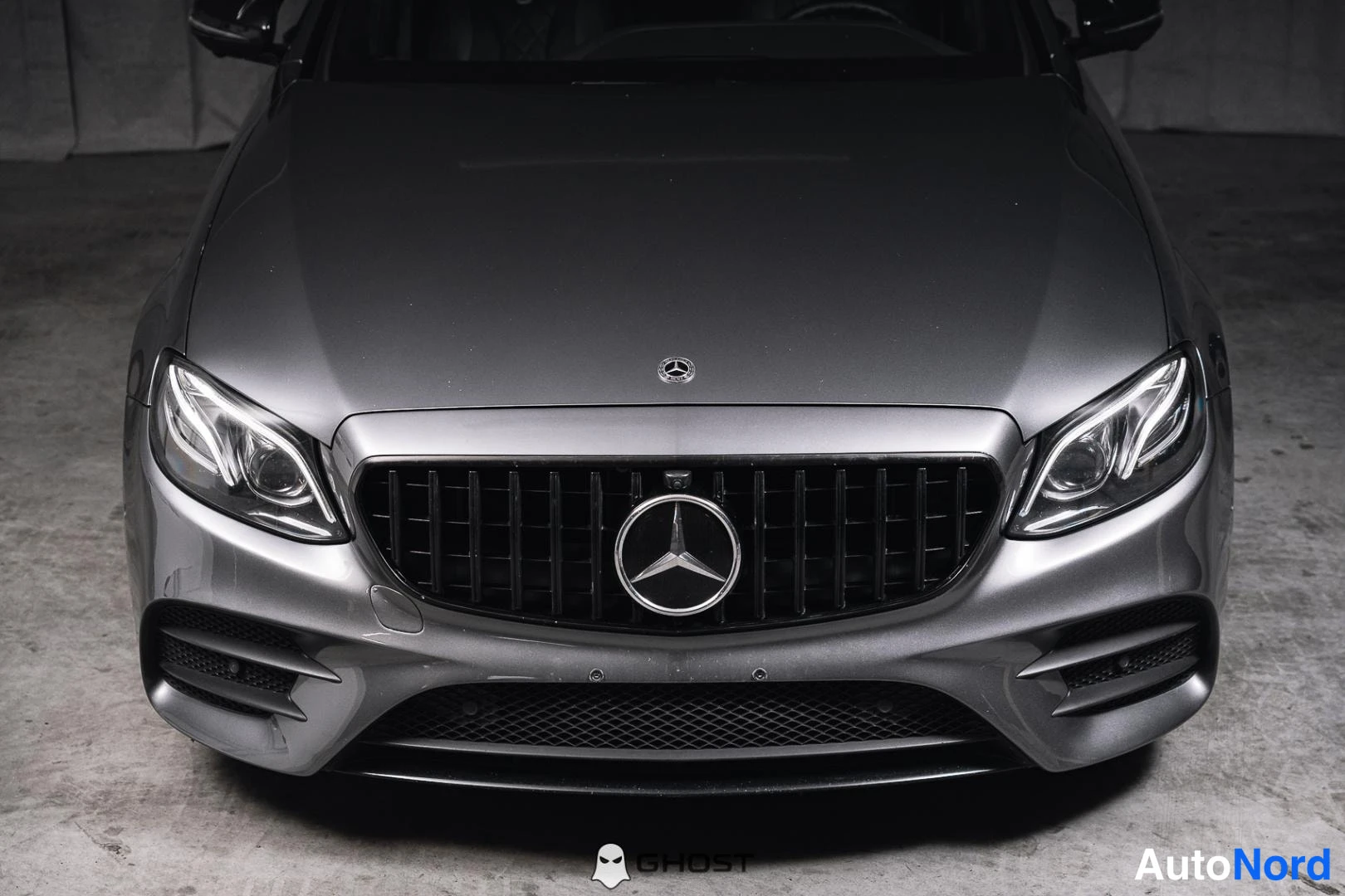 Edestä: Lähikuva harmaan Mercedes-Benzin keulasta: konepelti, pystysäleikkö tähdellä ja ajovalot.