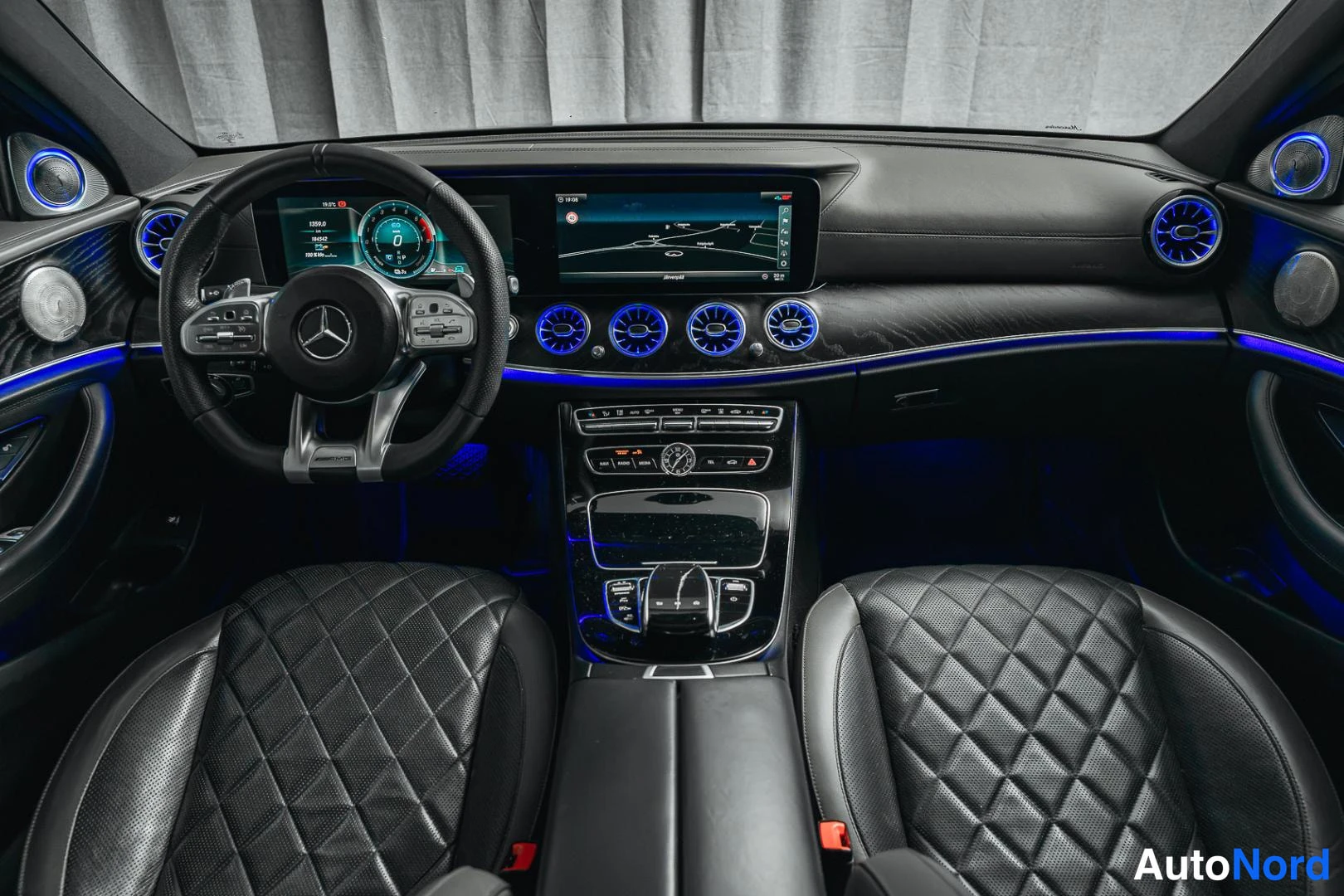 Sivulta: Mercedes-Benzin ohjaamo AMG-ohjauspyörällä, korinttiset urheiluistuimet, sininen tunnelavavalo, digitaalitane mittaristo ja suuri keskityön näyttö, Mercedes-Ben