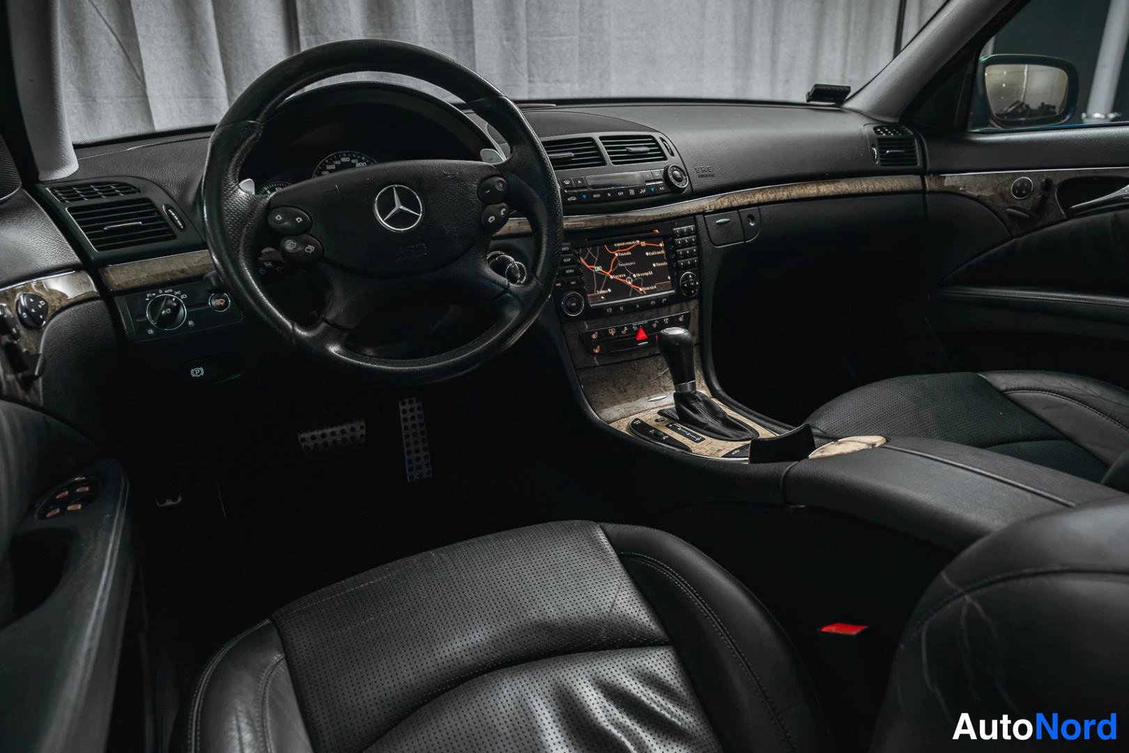 Etuistuimet: Interior view of the front cabin from the passenger side, featuring a multifunction steering wheel, a dashboard infotainment screen with a map, and black perfor