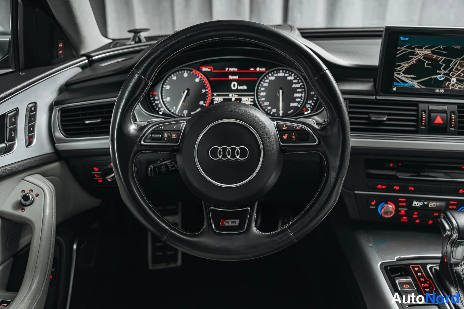 Muu: Rattitila lähikuvassa: Audi-logo ratin keskellä ja 'S6'-merkintä ratin alaosassa, taustalla tietokonenäyttö kartalla.