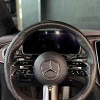 Yksityiskohta: Mercedes-Benz-ohjauspyörä tähtimerkillä keskellä, digitalisoitu mittaristo ja osa kojelaudasta taustalla.