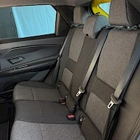 Muu: Auton takaistuimet harmaassa kankaassa, niskatuet ja turvavyöt näkyvissä; kuvassa myös takaojen alaosa ja ovipaneeli.