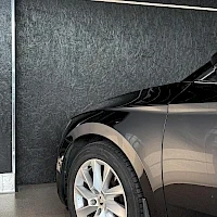 Sivulta: Kulmaus kuva tummanharmaan automobiilin etureunasta ja edessä olevasta pyörästä