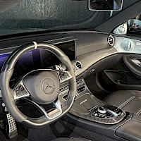 Ohjaamo: Sisäkuvan yläkulma, joka näyttää ohjauspyörän, mittariston, keskuspaneelin ja etutakat. Ohjauspyörässä on Mercedes-merkki ja sen päällä on pysty merkki.