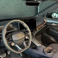 Ohjaamo: Wide shot of the dashboard from the driver's side perspective showing the steering wheel, a large central infotainment screen and door panel trim.