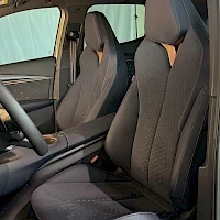 Etuistuimet: Front passenger seat view showing black fabric upholstery and headrest with an orange accent strip on the side bolster.