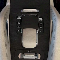 Etuistuimet: Center console control panel between seats showing silver-trimmed buttons including seat adjustment levers, cup holder area, and USB ports. Beige leather sides.