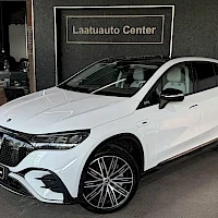 Etuviisto, nokka vasemmalle: Valkoinen Mercedes-Benz EQE SUV kuvattuna etukolmasosasta, nokka kuvan vasemmassa laidassa, taustalla Laatuauto Center -kyltti.