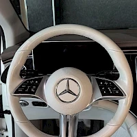 Edestä: Ohjauspyörän lähikuva sisältä: valkoinen ohjauspyörä, Mercedes-tähti ja monitoimipainikkeet, ilmanvaihtoaukot taustalla.