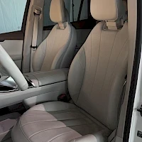 Etuistuimet: Front interior shot of the driver and front passenger seats. The seats are light beige or cream leather with black seatbelt buckles visible.