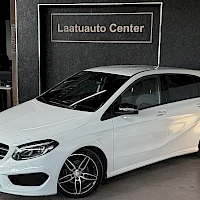 Etuviisto, nokka vasemmalle: Valkoinen Mercedes-Benz B 200 etuviistereunalta sisätiloissa; tummat kevytmetallivanteet, taustalla Laatuauto Center -kyltti.