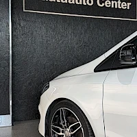 Sivulta: Kuvassa on valkoisen auton vasen etuosa, jossa näkyy pyörä ja kynnys. Taustalla musta seinä ja teksti 'Mantuauto Center'.