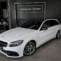 Etuviisto, nokka vasemmalle: Valkoinen Mercedes-Benz-farmari etukulmakuvassa vasemmalle suunnattuna; keula ja vasen sivu näkyvät, taustalla Laatuauto Center -kyltti.