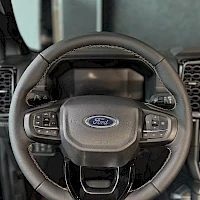 Yksityiskohta: Close-up of multifunction steering wheel with Ford logo, integrated control buttons on both spokes and digital display behind wheel rim