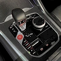 Ohjaamo: Center console area showing an automatic gear selector, start/stop button, infotainment knob, and carbon fiber trim