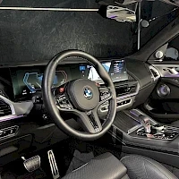 Muu: Ohjaamon näkymä: BMW-ohjauspyörä, kaareva leveä näyttö kojelaudassa ja automaattivaihteen valitsin keskikonsolissa.