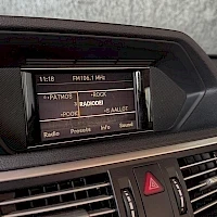 Muu: Kojelaudan keskikäyttöjärjestelmän näyttö, jossa näkyy radiovalikko kanavalista ja asetuksia, Mercedes-Benz-tyylinen sisätila.