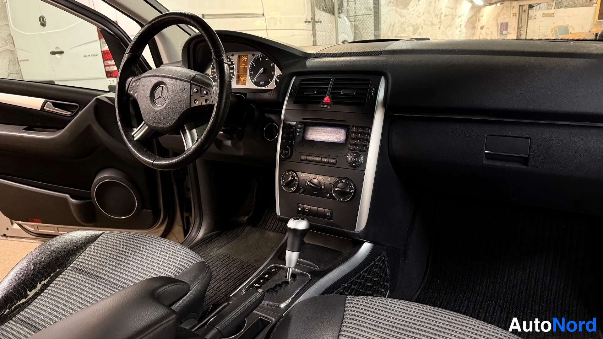 Yksityiskohta: Ajojärjestys kojelauta ja Mercedes-merkkinen ohjauspyörä, vaihteenvalitsin ja radio keskikonsolissa.
