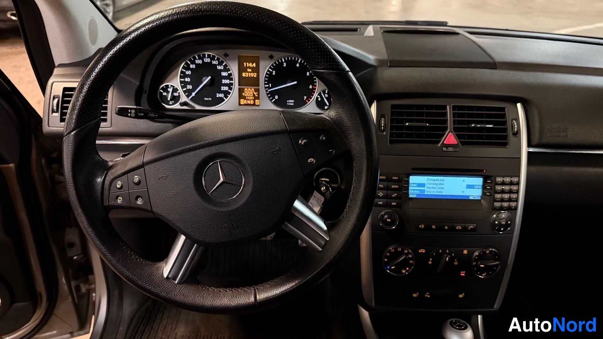 Yksityiskohta: Mercedes-ohjauspyörä ja kojelauta, mittaristo ja radiossa sininen näyttö.