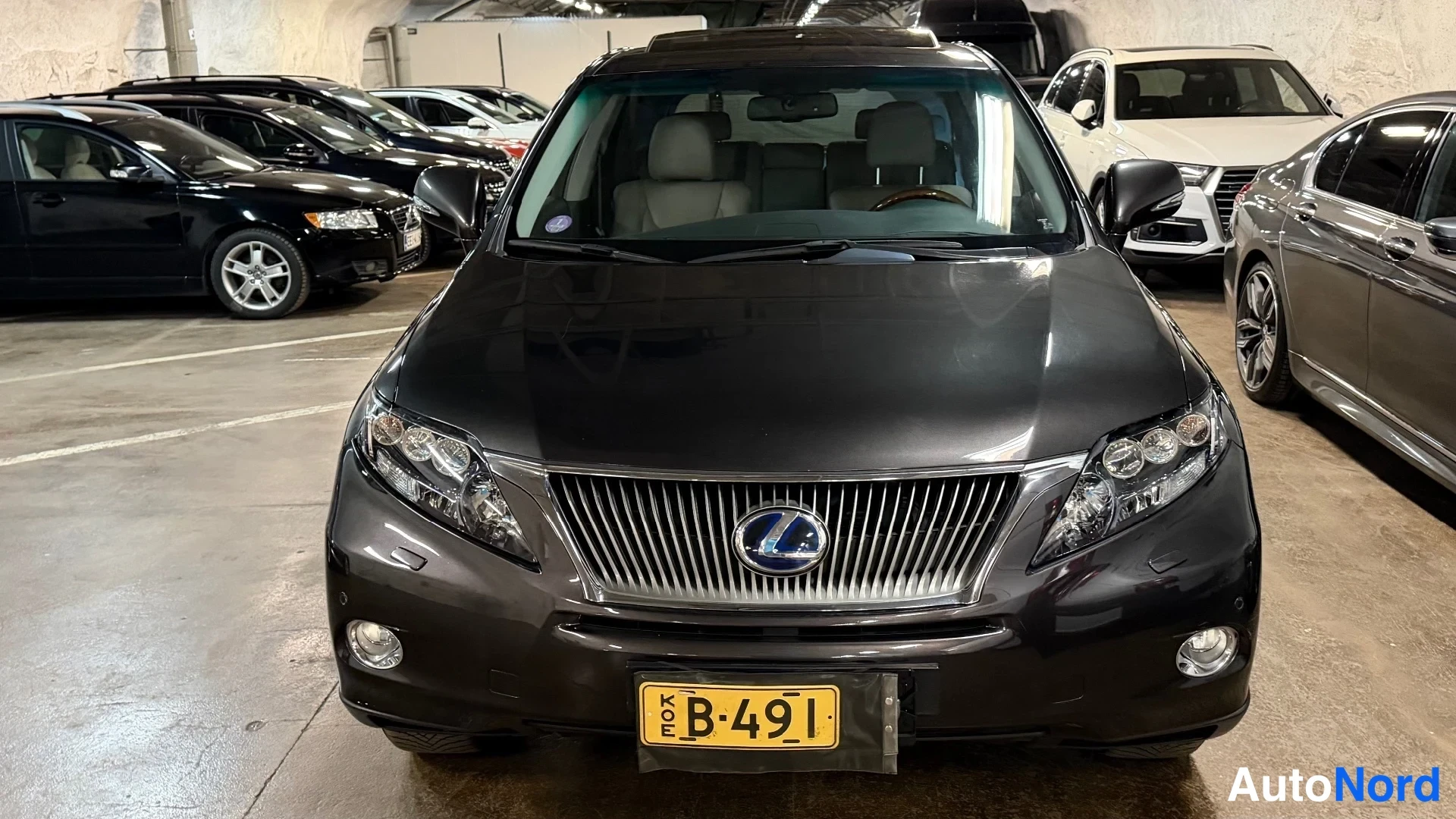 Edestä: Musta Lexus RX edestä päin, etukori ja rekisterikilpi KÖE B-491 näkyvät autotallissa.