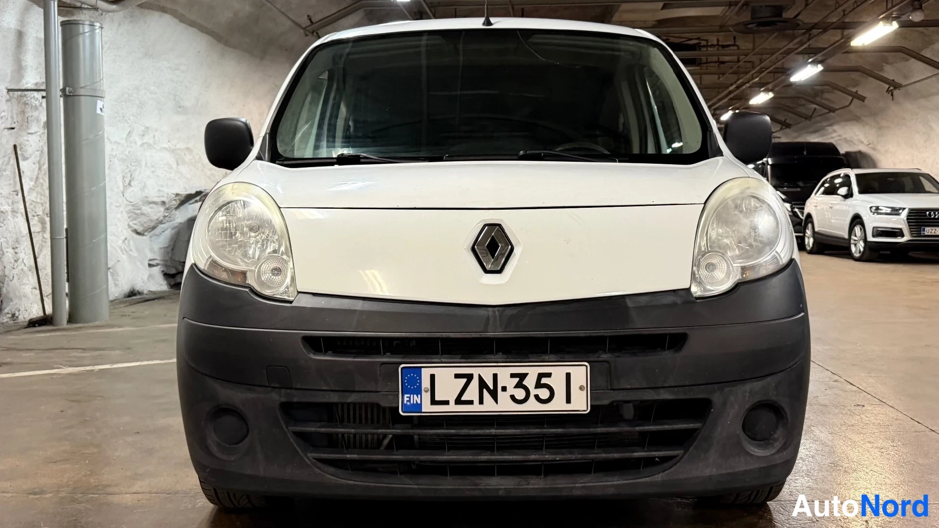 Edestä: Valkoisen Renault Kangoo -pakettiauton etunäkymä suoraan edestä, rekisterikilpi ja Renault-logo näkyvissä.