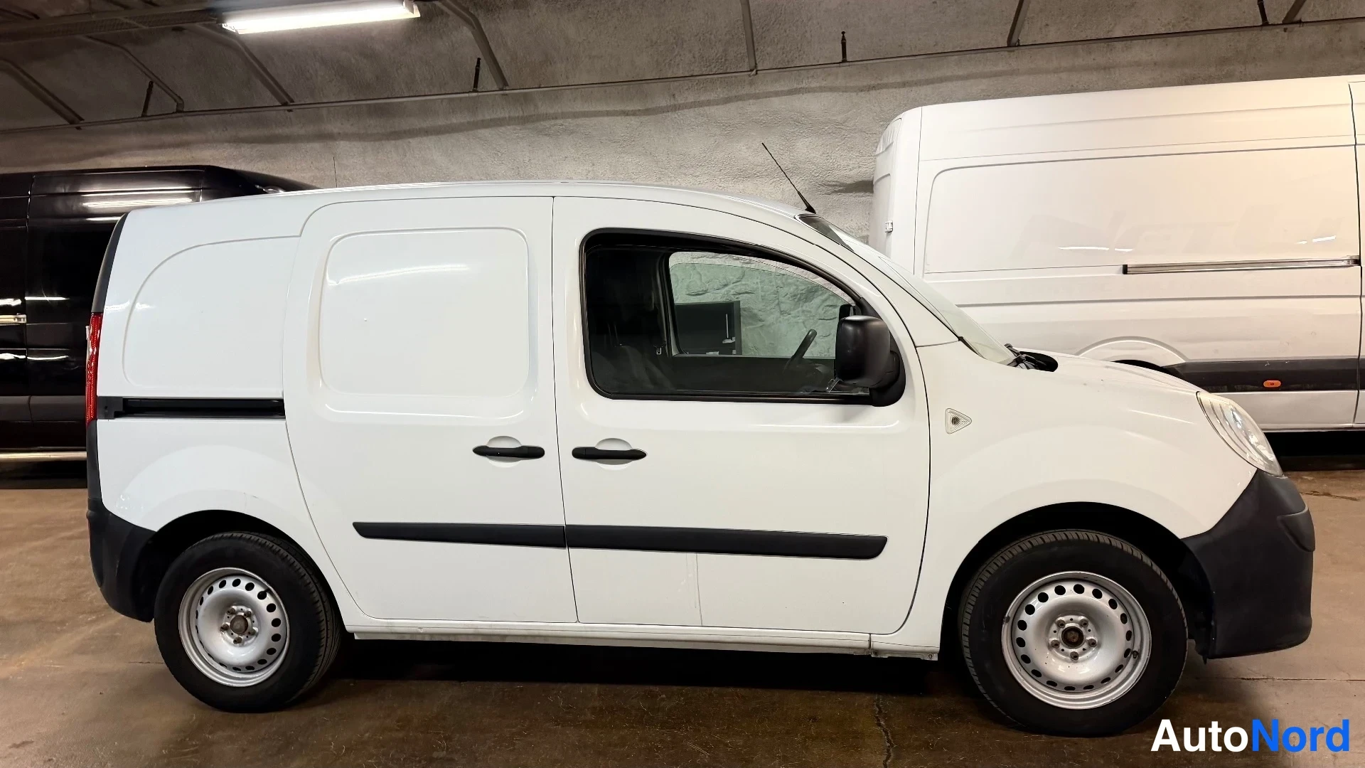 Sivulta: White Renault Kangoo Express van photographed from the side in a garage, showing both passenger and cargo door on the left flank, steel wheels, black bumper tri