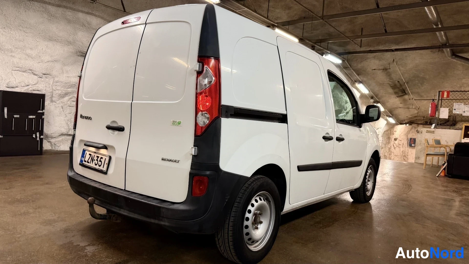 Takaviisto: Rear three-quarter view of a white Renault Kangoo Express van in a cave-like garage; rear face with red tail lights and 'RENAULT' badge visible, along with the