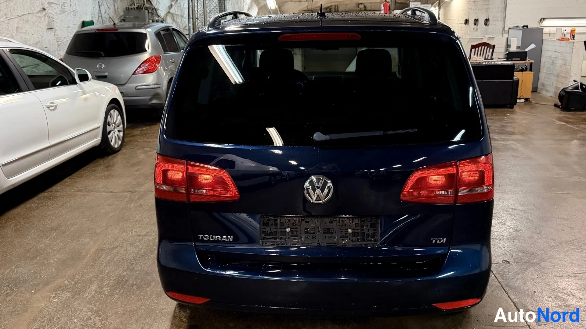 Takaa: Suora taka-kuva tummansinisestä Volkswagen Touranista. Takavalot ovat päällä.