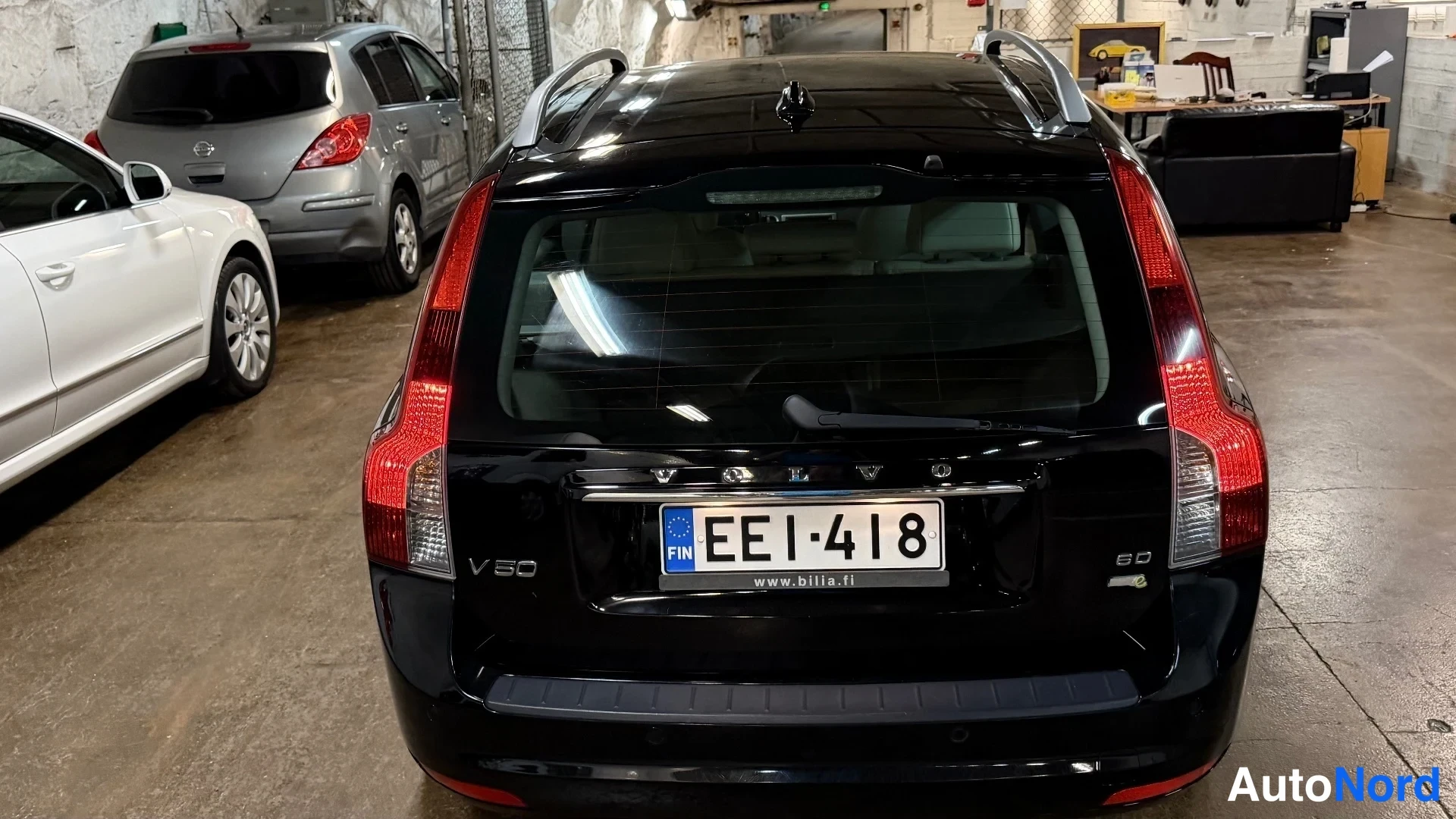 Takaa: Mustan farmarin takaosa suoraan takaa, rekisteritunnus, VOLVO- ja V50-merkinnät, kattokaiteet ja takalesli.