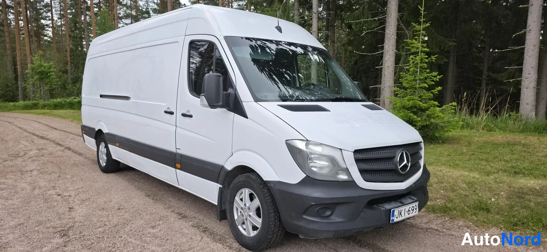 Etuviisto, nokka oikealle: Valkoinen Mercedes-Benz Sprinter -pakettiauto kolmivartalo-otteesta edestä oikealta; etusäleikkö Merkced-tähdellä, ajovalot ja rekisterikilpi JK I-699 nä