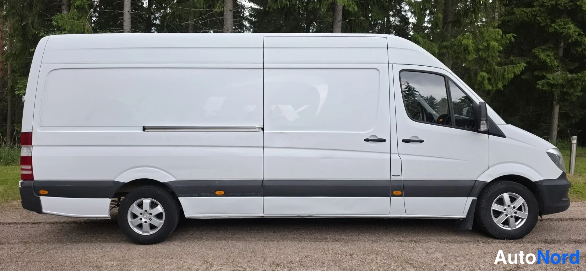 Sivulta: White van viewed from the right side. Sliding door handle visible on both sides of the panel. Black protective cladding along the bottom of the body.