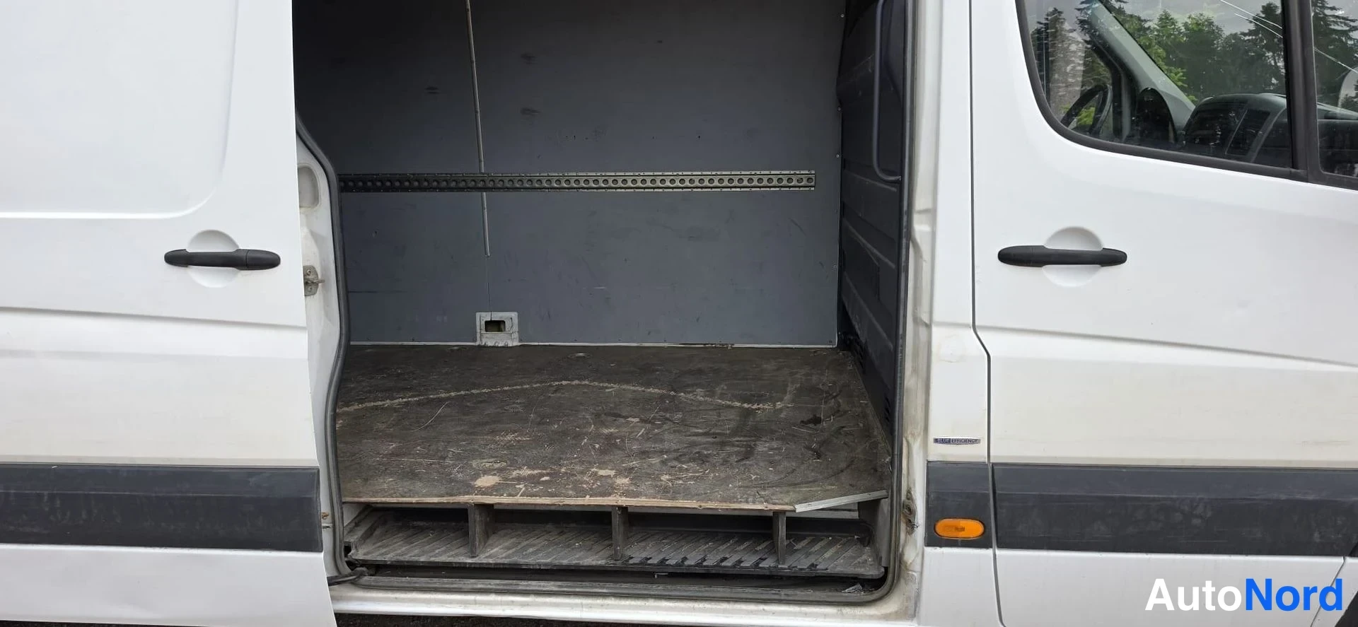 Sivulta: Pakettiauto sivulta, liukuovi auki ja tyhjä kuormatila näkyvissä; autossa kaksiovet ja väliseinä, ulkopuoli valkoinen.
