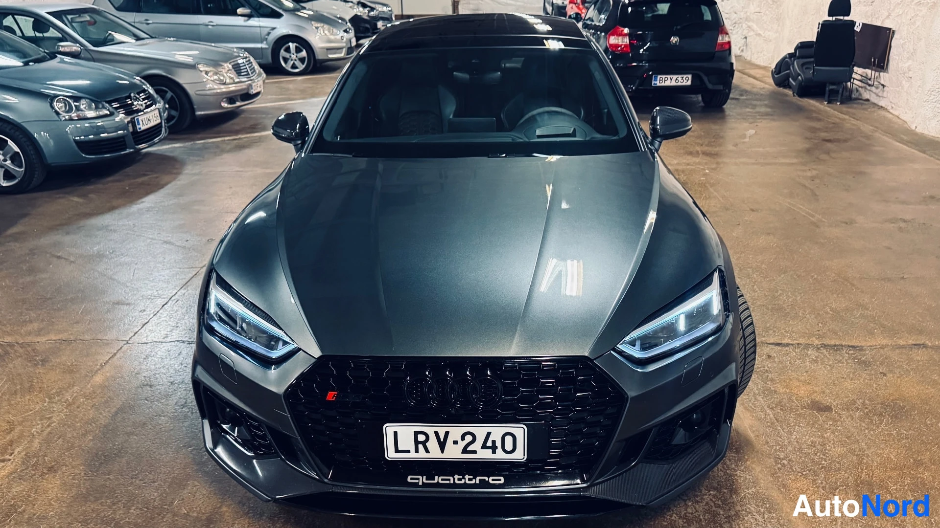 Edestä: Front view of a grey car with black honeycomb grille and LED headlights.