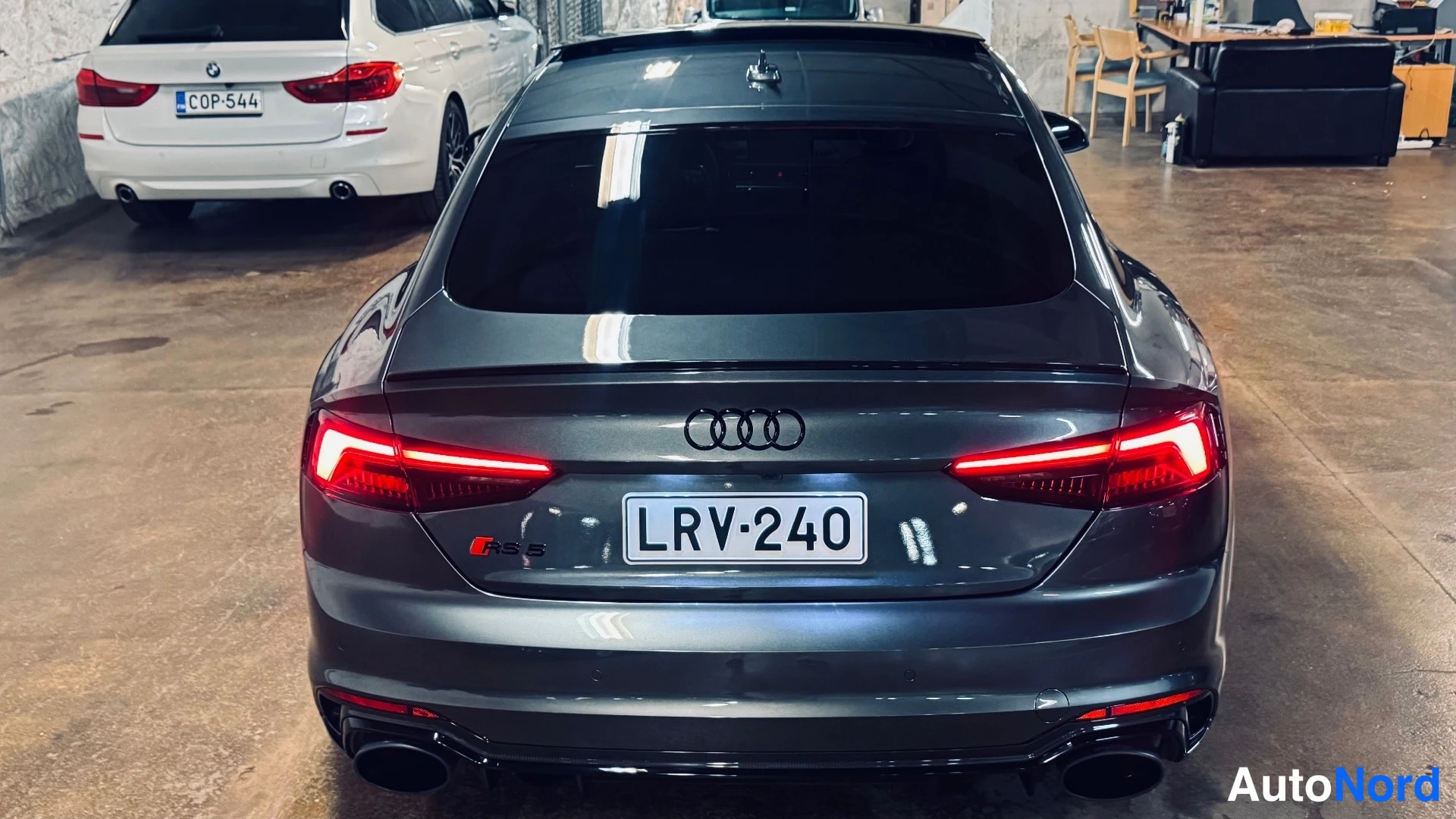 Takaa: Auton takaosa tummassa metallisävyssä, rekisteritunnus, Audi-renkaat ja neljä pakoputkea näkyvät.