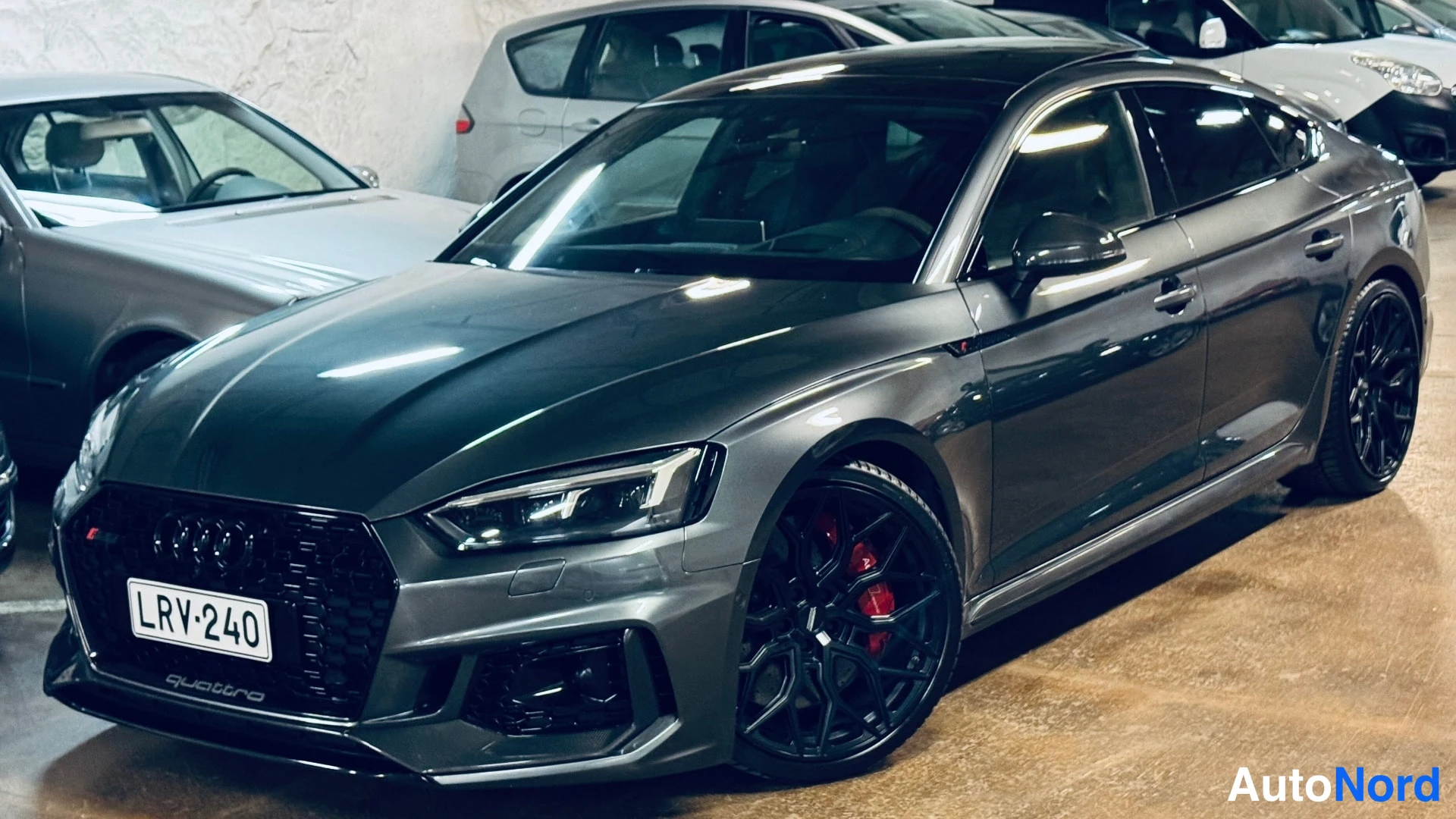 Etuviisto, nokka oikealle: Car angled to show the front right side. Black multi-spoke alloy wheels with red brake calipers visible.