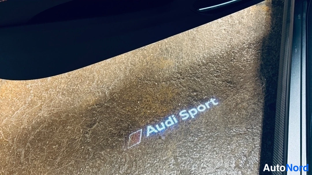 Sivulta: Oviaukkoon heijastettu Audi Sport -teksti tummassa sisätilassa
